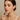 "Woman applying rose-colored lipstick, wearing natural glam makeup with soft eyeshadow and defined brows, name-brand women’s makeup modeled for elegant beauty against a neutral background