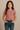 Smiling young girl wearing a dusty rose t-shirt and medium blue jeans, modeling name-brand girls’ clothing for everyday casual fashion against a neutral background