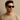 Young man wearing black wayfarer-style men’s sunglasses with dark lenses, name-brand fashion eyewear modeled against a neutral beige background."